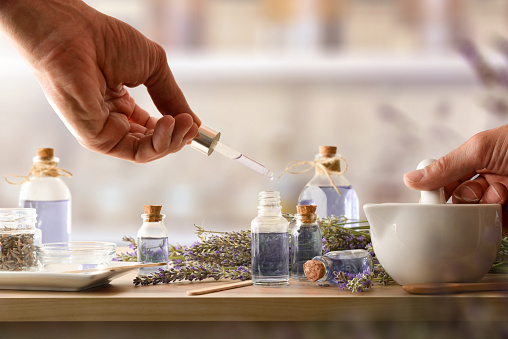 Person making homemade lavender essence with natural lavender spikes, jars and tools for the preparation on wooden table. Front view.