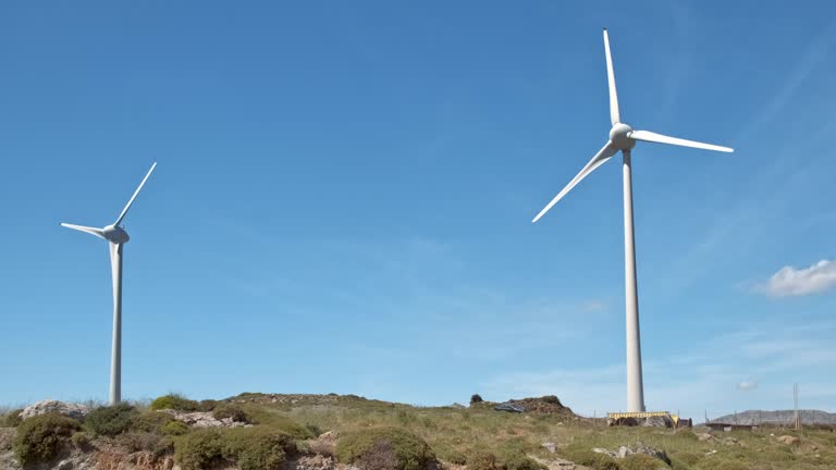 Diagonal shot of two wind turbines and road in-between in hill landscape on sunny day