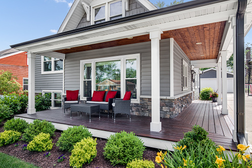 Oak Park, IL, USA - May 28, 2020: The exterior of a grey modern, suburban home with a covered porch and furniture featuring red accent pillows.