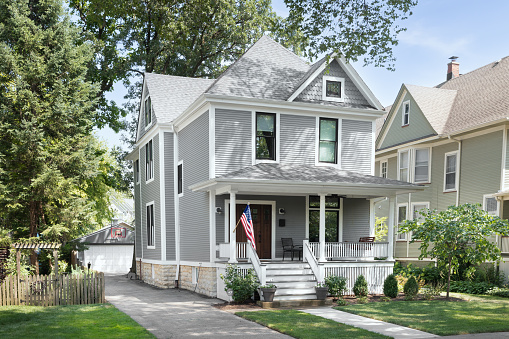 Chicago, IL, USA - August 1, 2020: A beautifully renovated Victorian home with a grey and white siding, a covered front porch and a driveway leading to the backyard.