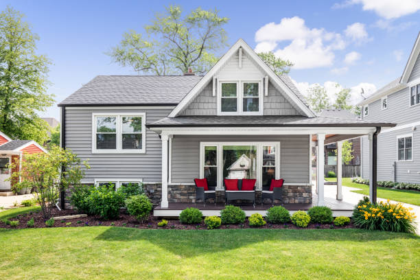 A grey modern farmhouse with a covered porch. Oak Park, IL, USA - May 28, 2020: The exterior of a grey modern, suburban home with a covered porch and furniture featuring red accent pillows. blue house red door stock pictures, royalty-free photos & images