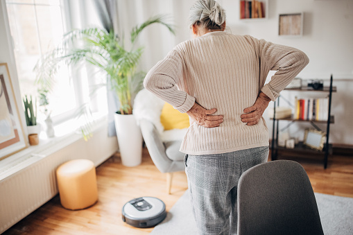 One woman, old woman having back pain while standing at home.