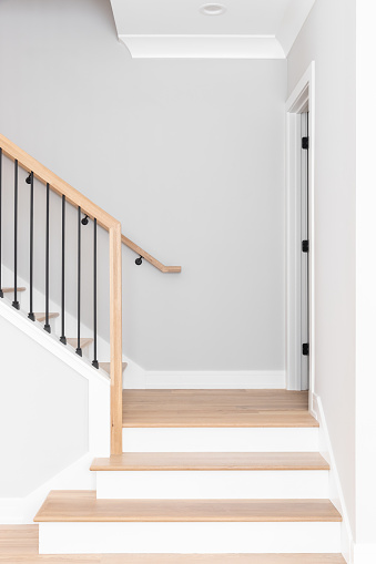 A staircase going up with natural wood steps and handrails, white risers, and wrought iron spindles.