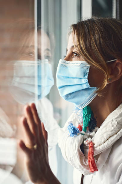istock profile view of a woman wearing a protective mask, looking through a window with her hand resting on the glass. concept of virus and confinement. 1452932647