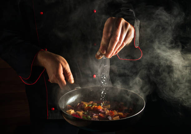 istock Cooking fresh vegetables. The chef adds salt to a steaming hot pan. Molecular cuisine menu idea for a hotel with advertising space 1452935045