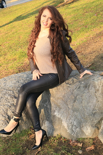 A Mexican model sitting on rocks on a sunny day in a public park in Autumn.