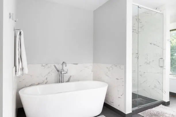 A luxury standalone bathtub and shower with marble walls and a dark tiled floor.