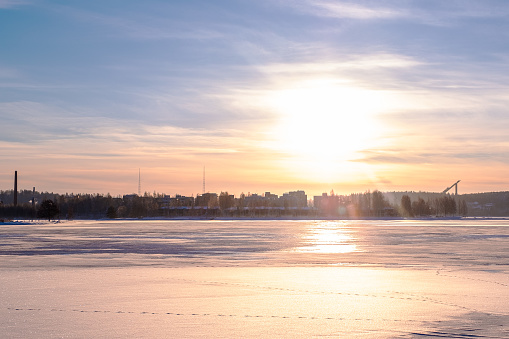 Winter cityscape at sunset. Frozen lake and city on the horizon in the rays of the sun.