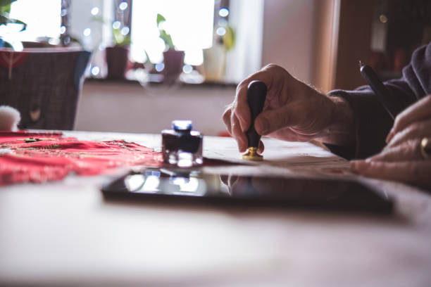 Senior man using pen and ink to write traditional letter and then sealing it with wax and stamp