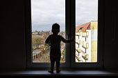 Lonely child standing on the windowsill. Dangerous situation, risk of falling out of the window