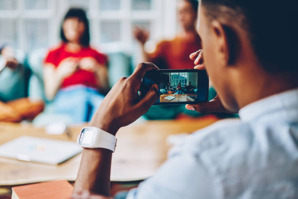 istock Ethnic man shooting with smartphone friends while resting together at home 1452948729