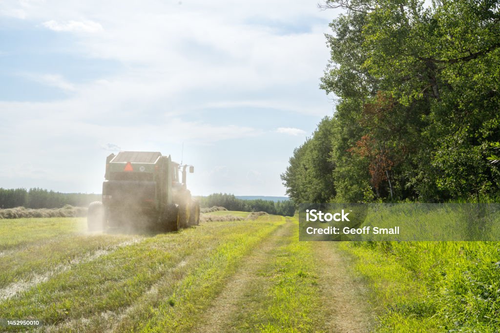 Tractor pulling a hay baler through a field A tractor driving away in a field, towing a baler Agricultural Field Stock Photo