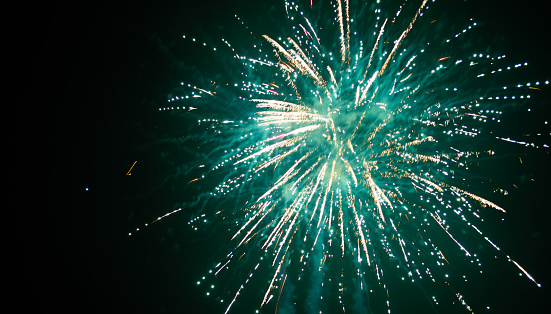 Bright fireworks against a night sky, colored green, along with yellow streaks of sparks and green smoke.