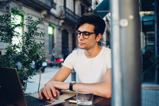istock Positive prosperous caucasian man blogger in eyewear for vision protection working remotely on laptop computer, handsome brunette hipster guy student watching video for education on cafe terrace 1452951459