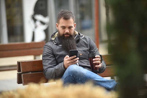 A shot of a bearded hipster man talking on phone and drinking coffee