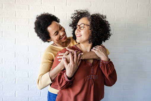 Smiling Latin-American woman embracing with her African-American wife in front of the white wall