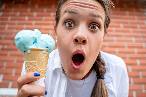 Young woman gasping and holding cone of blue ice cream