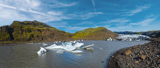 Solheimajokull glacier, Iceland. The tongue of this glacier slides from the volcano Katla. Beautiful glacial lake lagoon with blocks of ice and surrounding mountains. People unrecognizable.