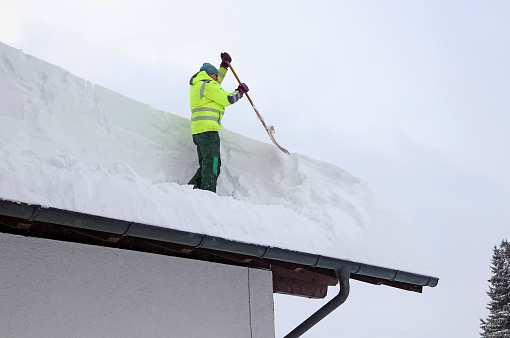 A man shoveling high heavy snow from a house roof