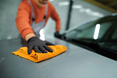 Close up shot of an unrecognizable professional car detailer cleaning car hood with microfiber towel
