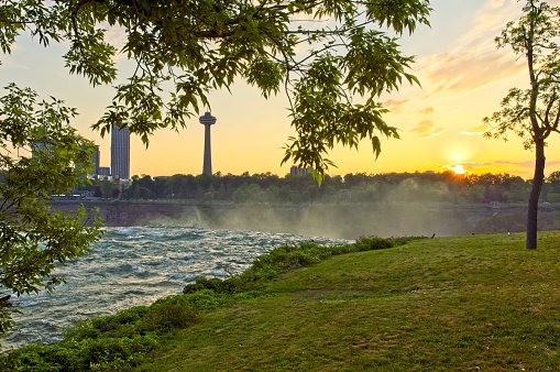Sunset at the edge of Niagara Falls with the spray rising and the Canadian side cityscape in the distance.