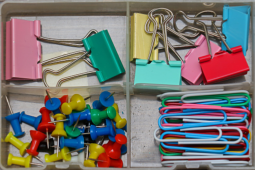 Colorful paper clips and pins stationery supplies inside plastic box