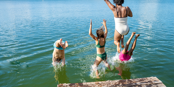 Multiracial group of people jumping into lake.