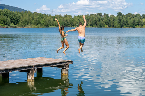 Young couple enjoying their vacations and jumping into the lake.