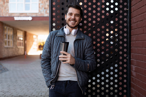 stylish man 35 years old in headphones with a glass of coffee looking at the camera on the street.