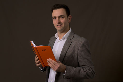 Concept new year resolution. Handsome entrepreneur reads business plan on 2023 orange agenda. Looking at camera. High quality photo