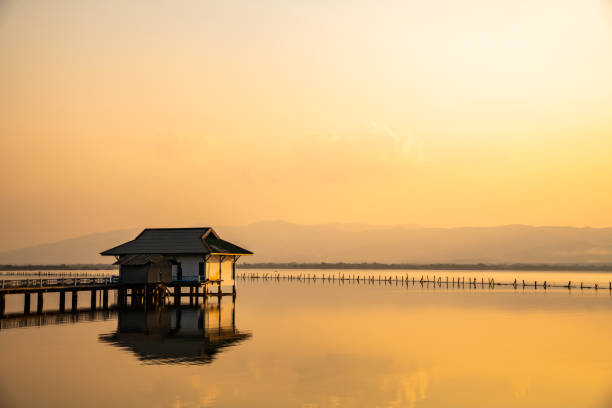 Fisherman on a wooden boat during a peaceful sunset over rippling waters in Myanmar, creating an atmosphere of quiet contemplation and natural beauty, with warm golden hues reflected across the tranquil landscape.