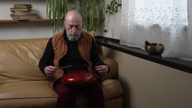 senior man is playing steel tongue drum with mallets