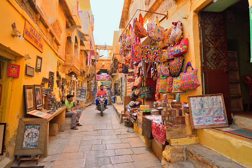 Jaisalmer, India - November 08, 2017: A man riding a scooter in the colorful streets inside jaisalmer fort.