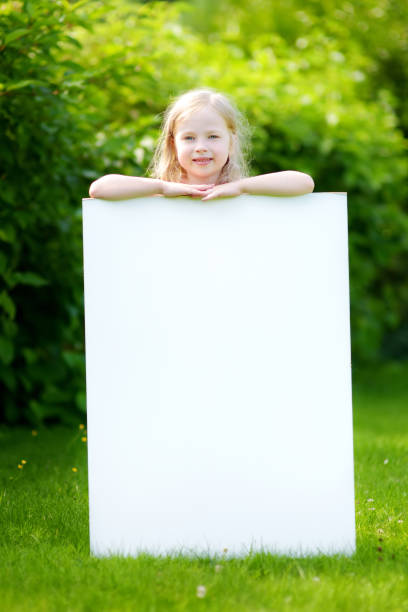 cute little girl holding big blank whiteboard on sunny summer day outdoors - preschooler childhood outdoors cheerful imagens e fotografias de stock