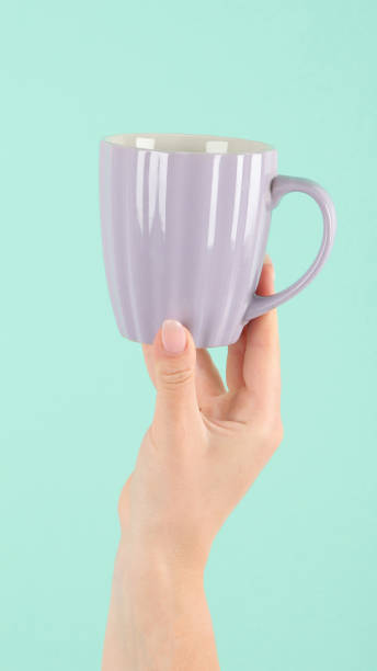 istock Arms raised up holding tea cup on green background. 1453025001