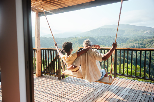 Rear view of a couple sitting together on a swing and looking at the scenic view from the balcony of their vacation rental
