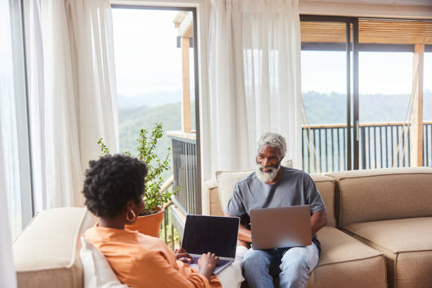 istock Smiling couple using laptops in their living room with a scenic view 1453028499