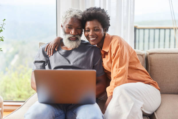 istock Smiling couple using a laptop in their living room overlooking a scenic view 1453028535