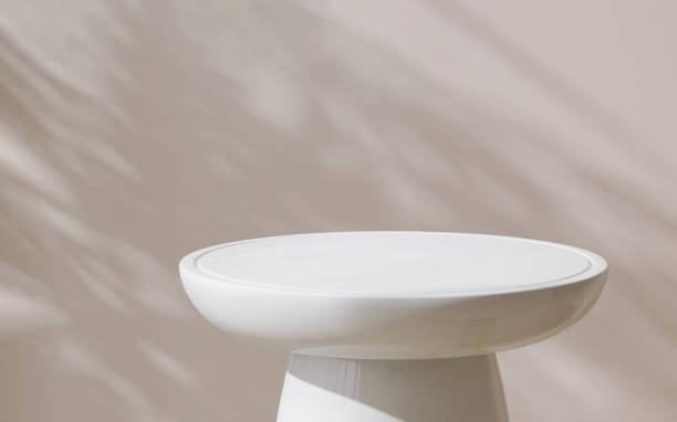 istock Modern, minimal round glossy white rock side table podium in dappled sunlight and leaf shadow on beige wall background 1453041164