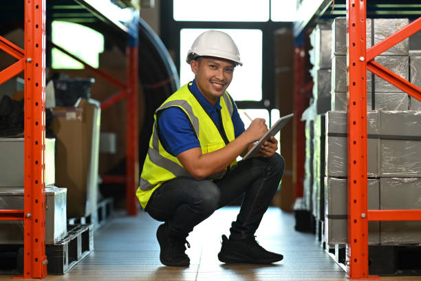istock Smiling warehouse worker sitting in aisle between rows of tall shelves full of packed boxes and using tablet. 1453044810