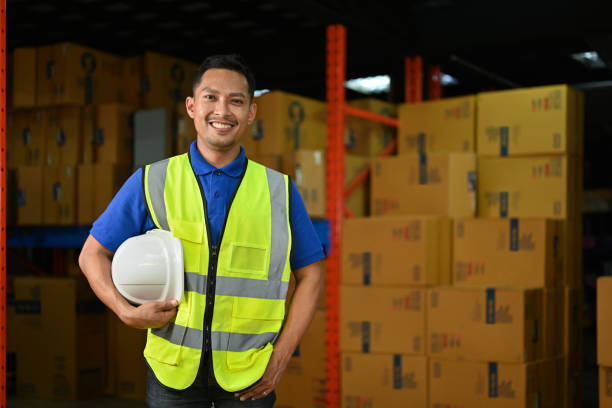 Industrial manager in yellow vest and holding hard hat in hand standing in a large warehouse. stock photo