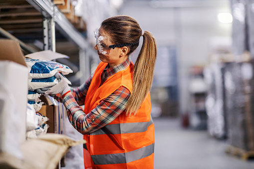 A warehouse worker collecting bags with salt or sugar in facility.