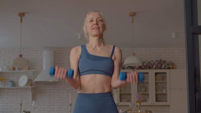 Pretty sporty fit senior woman doing dumbbell bicep curls exercise at home