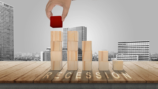 Businessman's hand build stairs from wooden blocks with recession signs with cityscape background