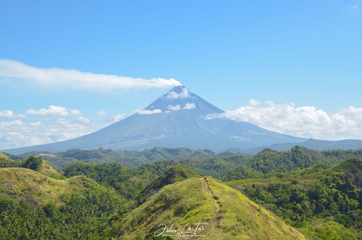 A scenic view of the Mayon Volcano surrounded by greenery on a sunny day