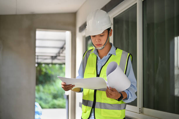 istock Architect man in safety helmet and reflective vest working with blueprint at construction site. 1453046621