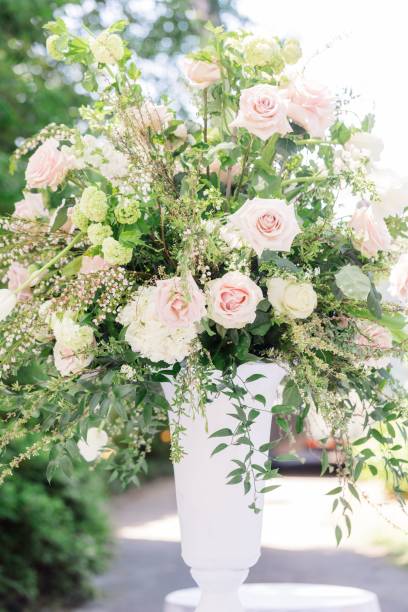 istock Composition of white roses, hydrangeas and green branches in a white vase under the rays of the sun 1453048033