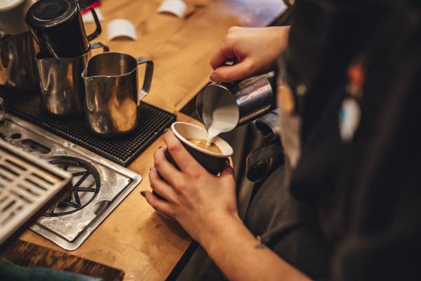 barista femminile che versa il latte per preparare una tazza di caffè cappuccino in una caffetteria - milk morning adult women foto e immagini stock