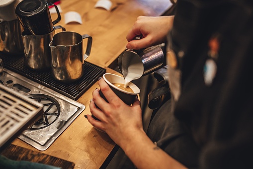A female barista pouring milk to make a cup of cappuccino coffee in a coffee shop