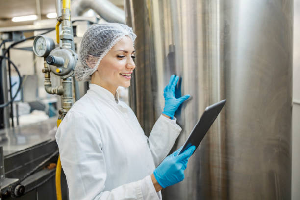 un operaio di un caseificio sta controllando la macchina per la lavorazione del latte e sorride al tablet. - color image food dairy product people foto e immagini stock